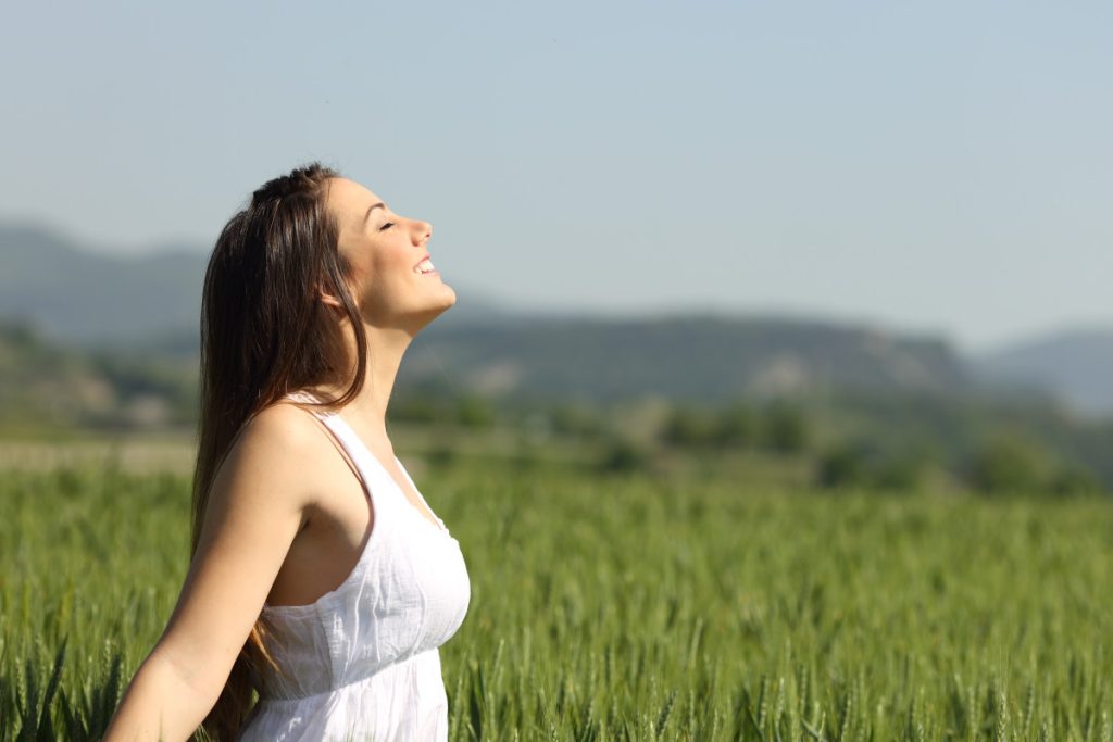 Girl breathing fresh air with white dress in a green wheat meadow